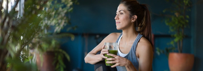 A woman holding a green smoothie while she sits and smiles.